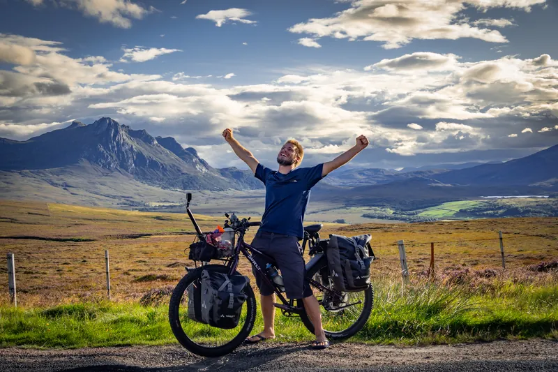 Arms raised next to a loaded touring bike in the Highlands